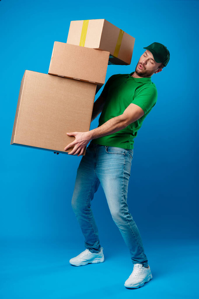 Παράδοση άνθρωπος με τεράστιο σωρό από κουτιά σε μπλε φόντο - Φωτογραφία, εικόνα