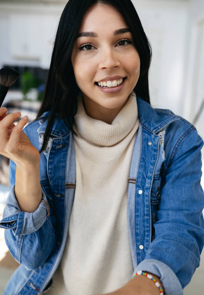 vertical photo of beautiful hispanic latin woman, putting on makeup at home, cowgirl casual clothes - Foto, Imagem
