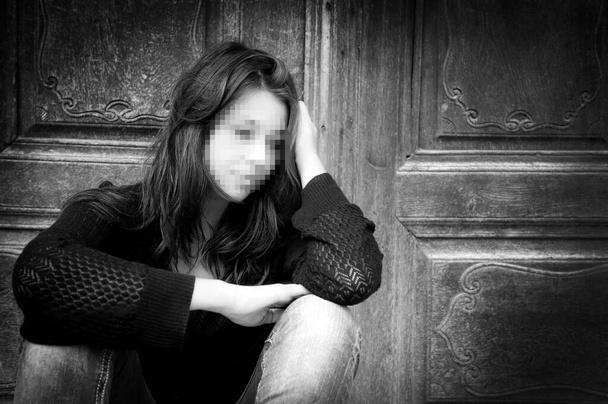 Foto en blanco y negro de una triste joven anónima con cara pixelada que reflexiona sobre los problemas frente a una pared gris - Foto, Imagen