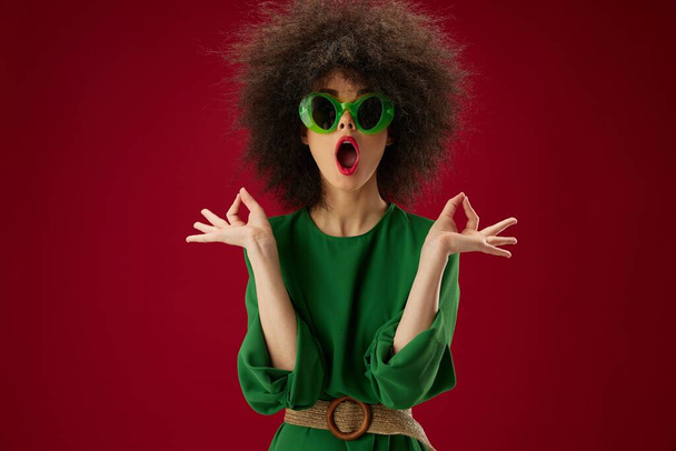 γυναίκα σε πράσινο φόρεμα γυαλιά ηλίου μόδα χτένισμα κόκκινο φόντο - Φωτογραφία, εικόνα