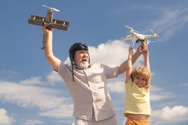 Young grandson and old grandfather playing with toy plane and quadcopter drone against sky. Child pilot aviator with plane dreams of traveling. Family Relationship Grandfather and child. - Photo, image