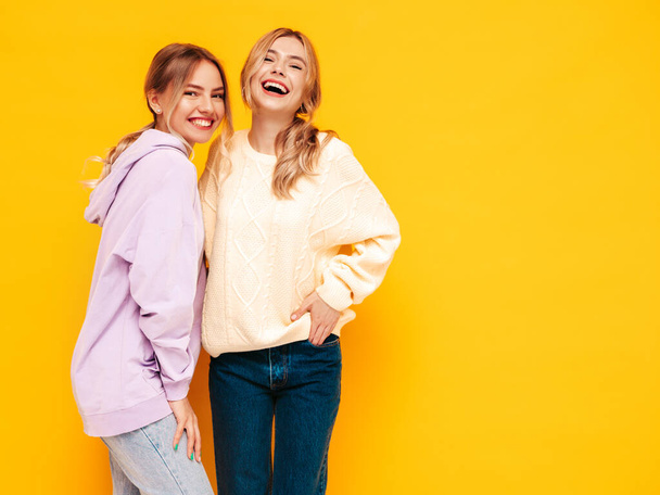 Dos jóvenes guapas y sonrientes morena hipster hembra en ropa de verano de moda. Sexy mujeres despreocupadas posando cerca de la pared amarilla en el estudio. Modelos positivos divirtiéndose. Alegre y feliz - Foto, imagen