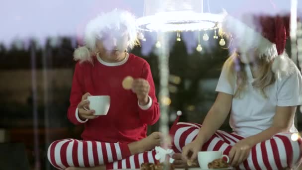 Zwei Kinder mit Weihnachtsmützen sitzen, trinken Tee und essen zu Hause zu Weihnachten Kuchen    - Filmmaterial, Video