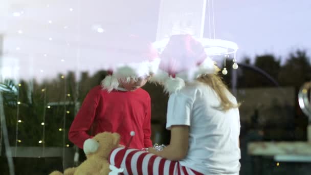 Deux enfants portant des chapeaux de Noël assis avec des boîtes-cadeaux à la maison à la période de Noël  - Séquence, vidéo