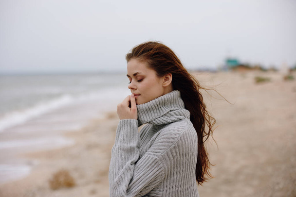 Fröhliche Frau im Pullover mit wehenden Haaren am Meer - Foto, Bild