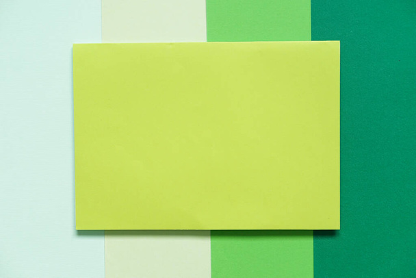 bovenaanzicht van een blanco groen A4 papierformaat op een groene achtergrond met verschillende tinten groen, kopieer ruimte - Foto, afbeelding