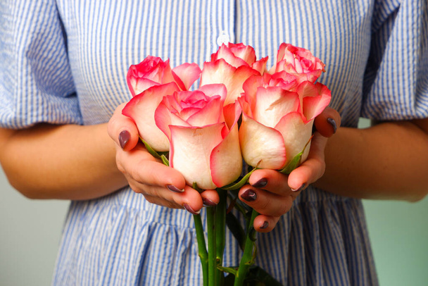 Mujer en vestido azul sosteniendo delicada flor rosa en las manos. Primeros planos de las manos de la mujer con manicura blanca con delicada flor rosa - Foto, Imagen