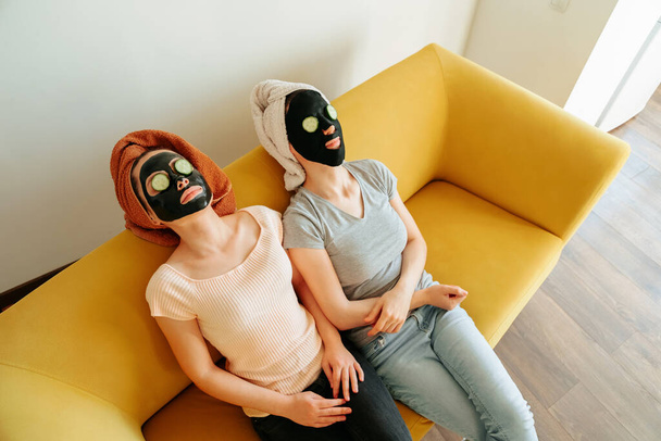 top view of a two young woman lying with cosmetic masks on their faces and cucumber - Fotó, kép