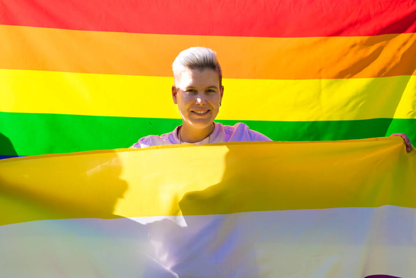 La persona non binaria di genere è con la bandiera dell'orgoglio gay sullo sfondo sulla spada e la bandiera non binaria sul davanti. Concetto di non binario e androgino. Diversità e orgoglio gay. - Foto, immagini