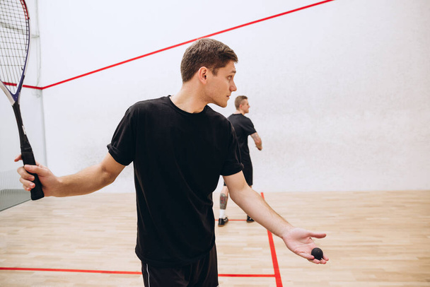 Cropped portrait of young man playing squash game, praparing to serve ball with racket isolated over sport studio backround - Zdjęcie, obraz