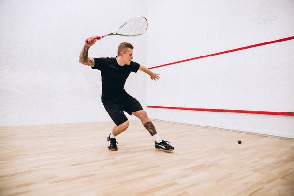 Teljes hosszúságú portré fiatal sportoló férfi fekete egyenruha képzés, játszik squash a sport stúdió - Fotó, kép