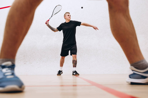 Retrato de deportista, joven jugando squash, sirviendo pelota aislada sobre fondo de estudio deportivo - Foto, Imagen