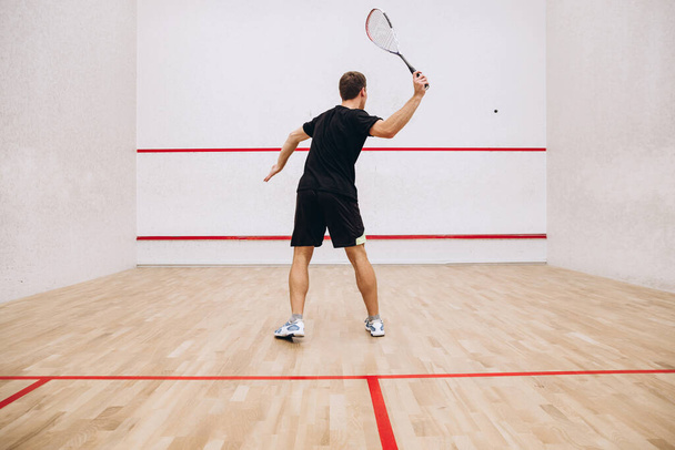 Back view of man playing squash game alone in sport studio - Photo, Image
