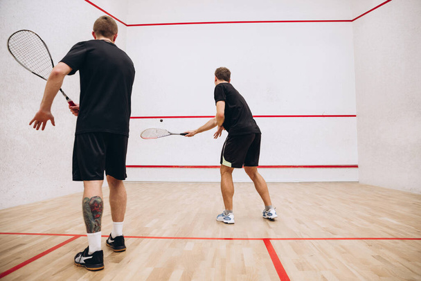 Ganztägiges Porträt zweier junger sportlicher Männer, die in einem speziellen Sportstudio Squash spielen. Rückseite - Foto, Bild
