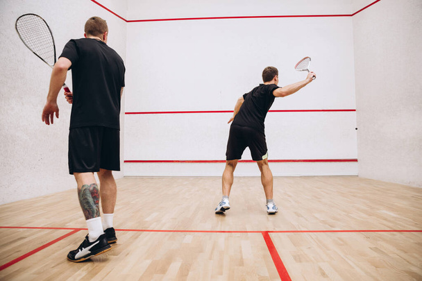Ganztägiges Porträt zweier junger sportlicher Männer, die in einem speziellen Sportstudio Squash spielen. Rückseite - Foto, Bild