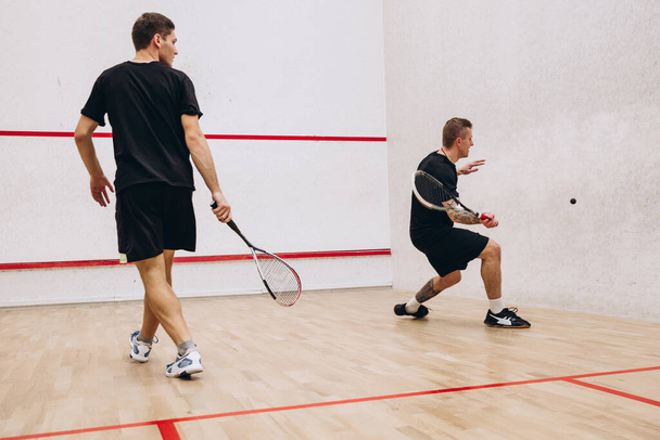 Full-length portrét dvou mladých sportovních mužů trénink, hrát squash hru ve speciálním sportovním studiu. Zadní pohled - Fotografie, Obrázek
