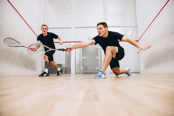 Retrato de larga duración de dos jóvenes deportistas entrenando juntos, jugando squash aislado sobre fondo de estudio deportivo - Foto, Imagen