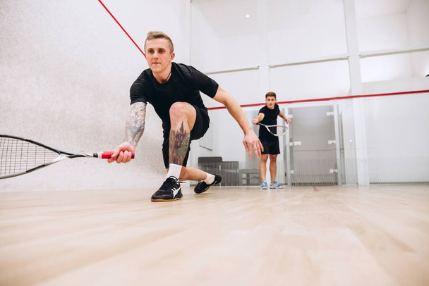Spor stüdyosunun arka planında izole edilmiş squash oynayan iki genç sporcunun tam boy portresi. - Fotoğraf, Görsel
