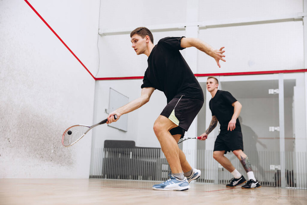 Full-length vista laterale ritratto di due giovani ragazzi in movimento, giocare a squash isolato su sfondo studio sportivo - Foto, immagini