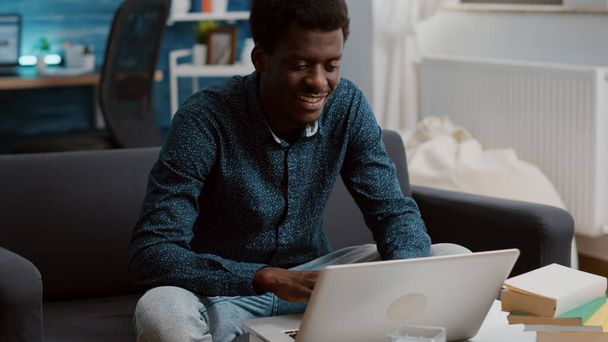 Authentisch lächelnder schwarzafrikanisch-amerikanischer Typ, der von zu Hause aus an seinem Laptop arbeitet - Foto, Bild