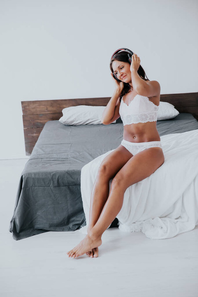 krásná žena ve spodním prádle poslech hudby se sluchátky v ložnici na posteli - Fotografie, Obrázek