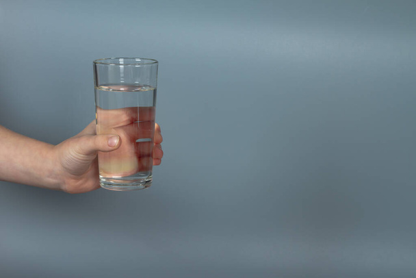 Мужчина держит стакан воды в руке на сером фоне в студии. - Фото, изображение