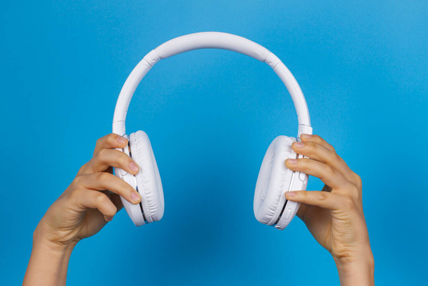 Mãos segurando modernos fones de ouvido sem fio brancos no fundo azul claro - Foto, Imagem