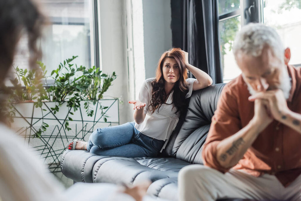 mulher preocupada falando com psicólogo turvo enquanto sentado no sofá perto do marido deprimido - Foto, Imagem