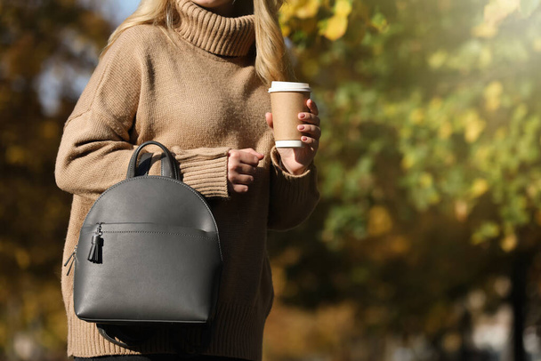 Young woman with stylish backpack and hot drink on autumn day, closeup. Space for text - Valokuva, kuva
