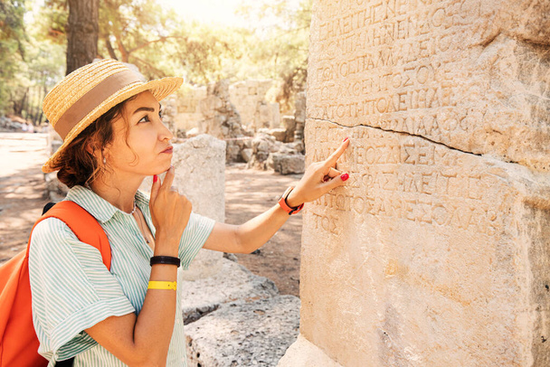 Vrouwelijke filoloog en toerist leest en probeert oud Grieks te vertalen uit zuilen in de ruïnes van een antieke stad. Taalkunde en archeologie - Foto, afbeelding