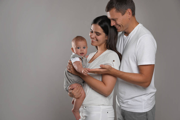 Happy family. Couple with their cute baby on grey background, space for text - 写真・画像
