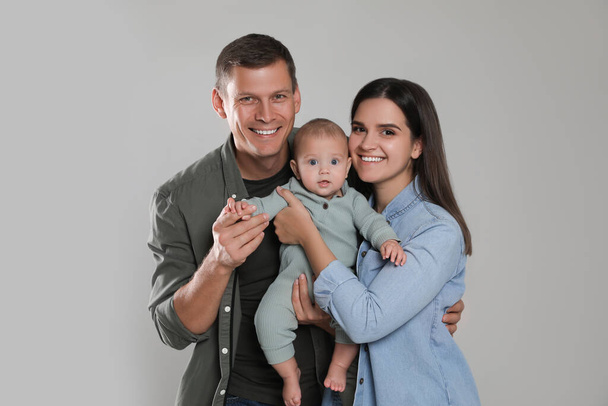 Happy family. Couple with their cute baby on grey background - Фото, изображение