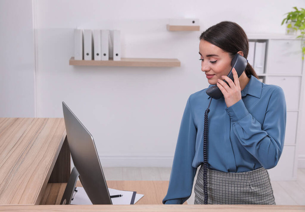Female receptionist talking on phone at workplace - Fotografie, Obrázek