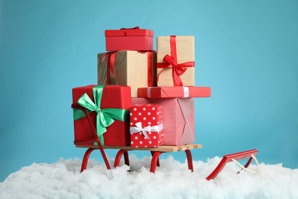 Сани с рождественскими подарочными коробками и искусственным снегом на светло-голубом фоне - Фото, изображение