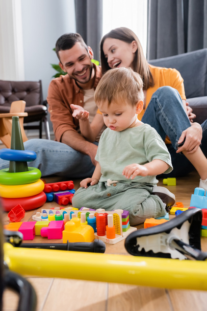 Toddler kid sitting near toys, bike and parents at home  - Fotó, kép