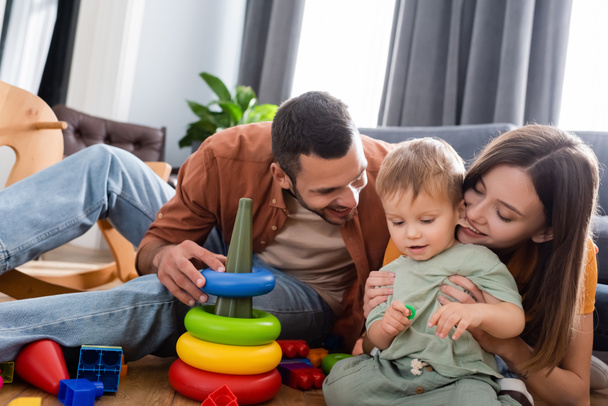 Cheerful parents sitting near son and toys in living room  - Foto, afbeelding
