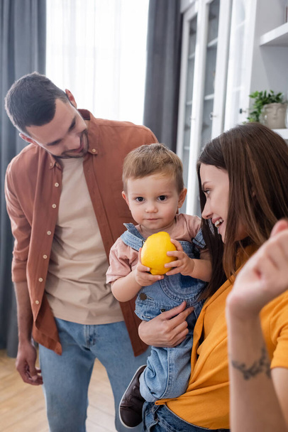 Toddler boy holding lemon near smiling parents at home  - Фото, зображення