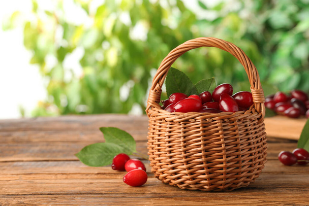 Fresh ripe dogwood berries with green leaves in wicker basket on wooden table, space for text - Foto, immagini