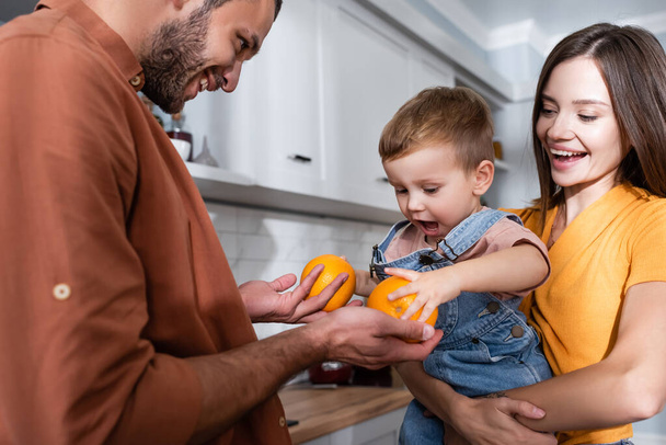 Man holding oranges near kid and wife at home  - Zdjęcie, obraz