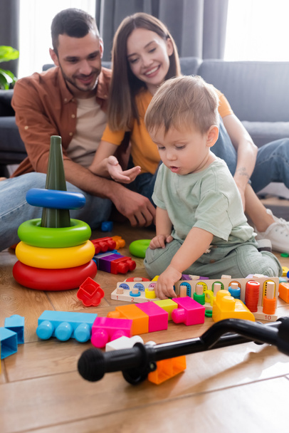 Kid playing with toys near blurred parents in living room  - Foto, Bild