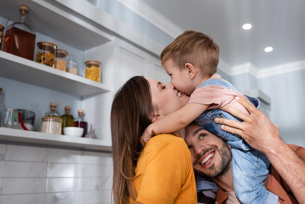 Smiling woman kissing son near husband at home  - Valokuva, kuva