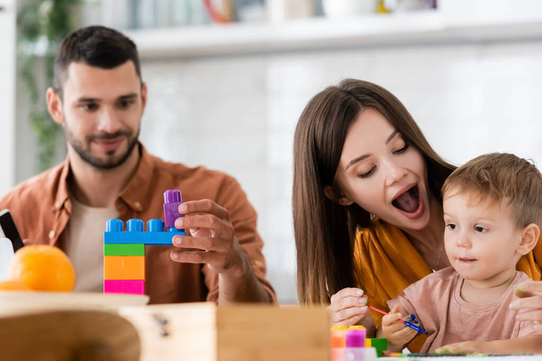 Woman holding paintbrush near son and husband with building blocks at home  - Foto, immagini