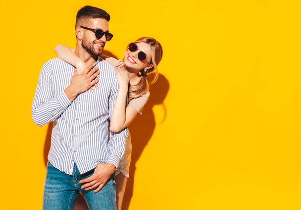 Sexy smiling beautiful woman and her handsome boyfriend. Happy cheerful family having tender moments near yellow wall in studio.Pure cheerful models hugging.Embracing each other in sunglasses - 写真・画像