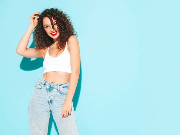 Young beautiful smiling female in trendy summer  hipster clothes. Sexy carefree woman posing near blue wall in studio. Positive brunette model with afro curls hairstyle. Cheerful and happy - Φωτογραφία, εικόνα