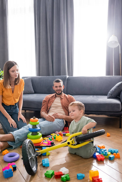 Parents spending time with toddler son holding bike in living room  - Foto, imagen