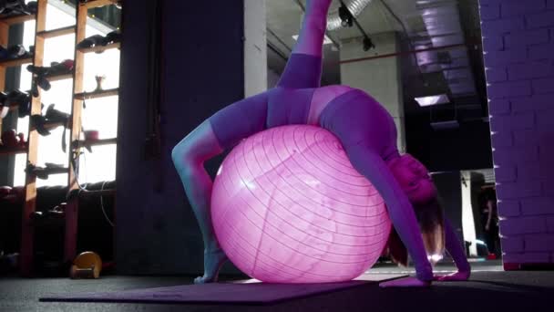 Mujer joven haciendo ejercicios de pilates ejercicio mientras está sentado en la pelota de fitness en la iluminación de neón - Metraje, vídeo