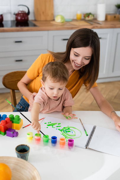 Smiling woman sitting near son drawing at home  - Photo, Image