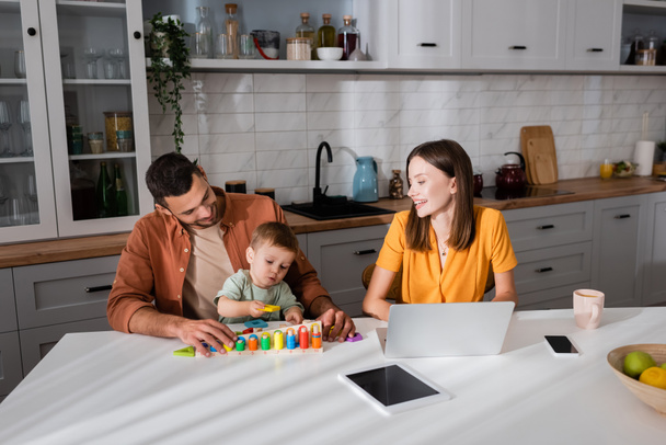 Férfi és gyerek játék közelében anya dolgozik laptop és gyümölcsök otthon  - Fotó, kép