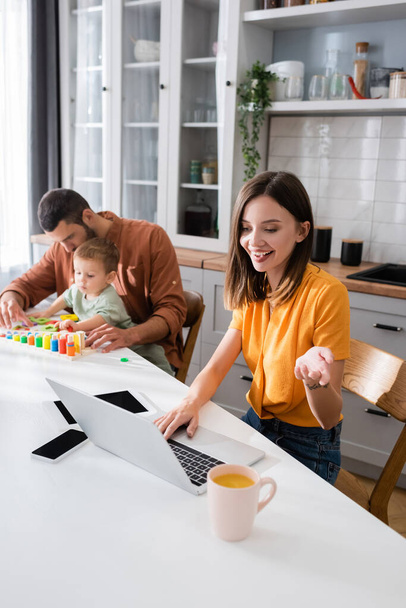Freelancer having video call on laptop near coffee and family at home  - Φωτογραφία, εικόνα