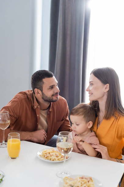 Parents looking at each other near son and delicious dinner at home  - Photo, image